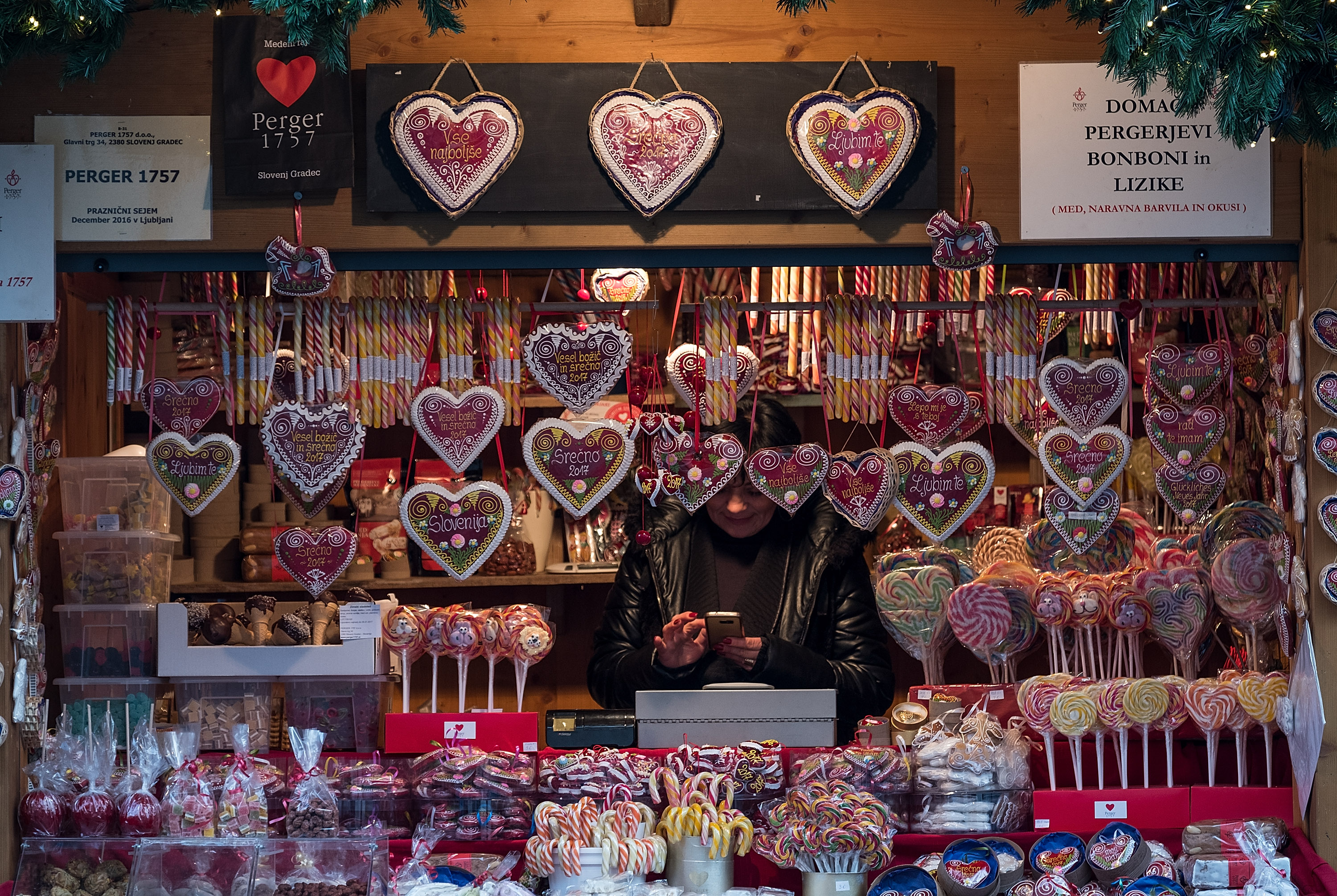A stall holder at a Christmas market in Ljubljana, Slovenia, shows traditional products including candy and heart-shaped gingerbread.