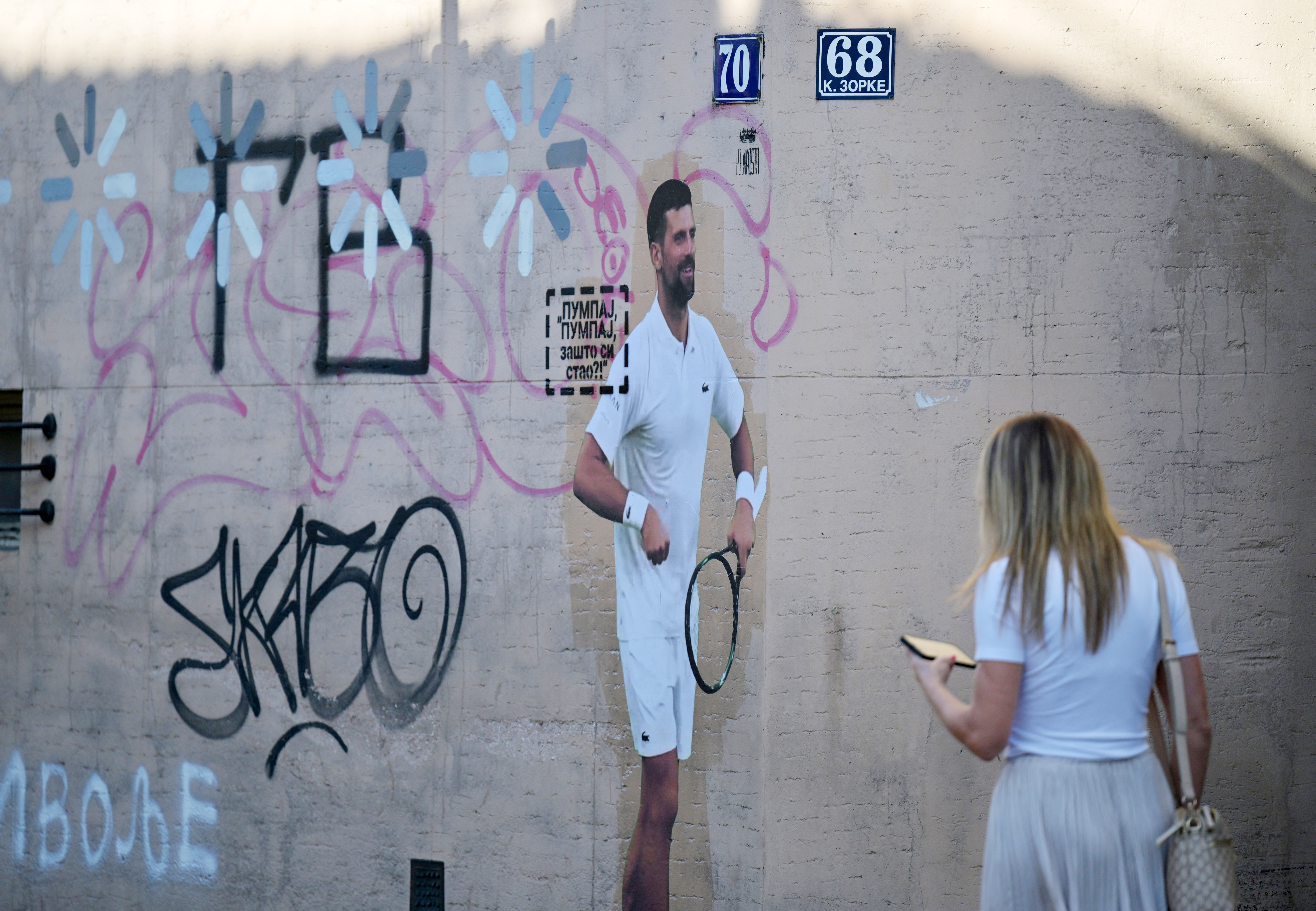 A pedestrian walks past a collage featuring an image of Serbian tennis player Novak Djokovic on a wall in Belgrade.
