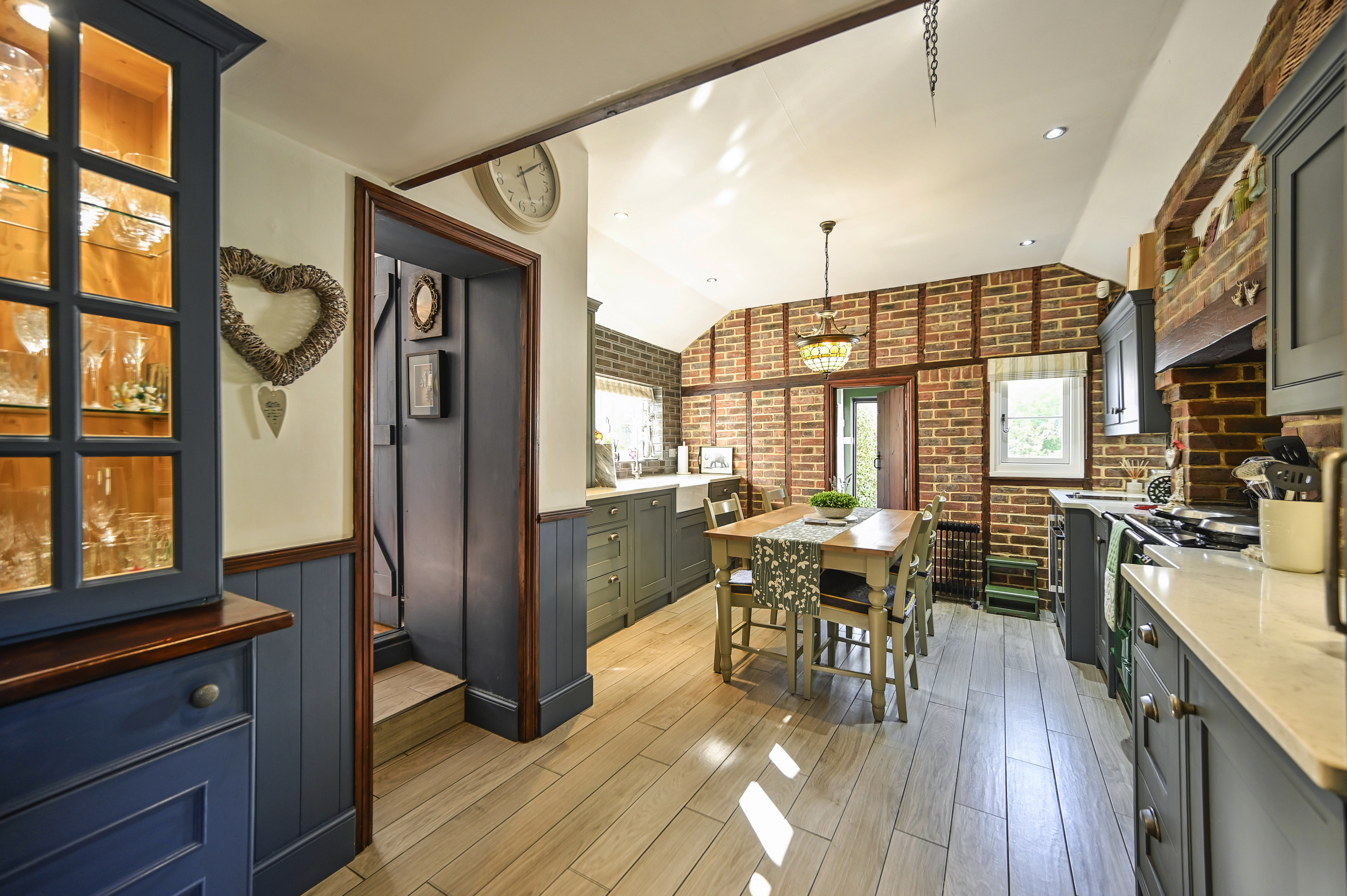 Kitchen with wooden table and four chairs, exposed brick walls, and grey cabinetry.