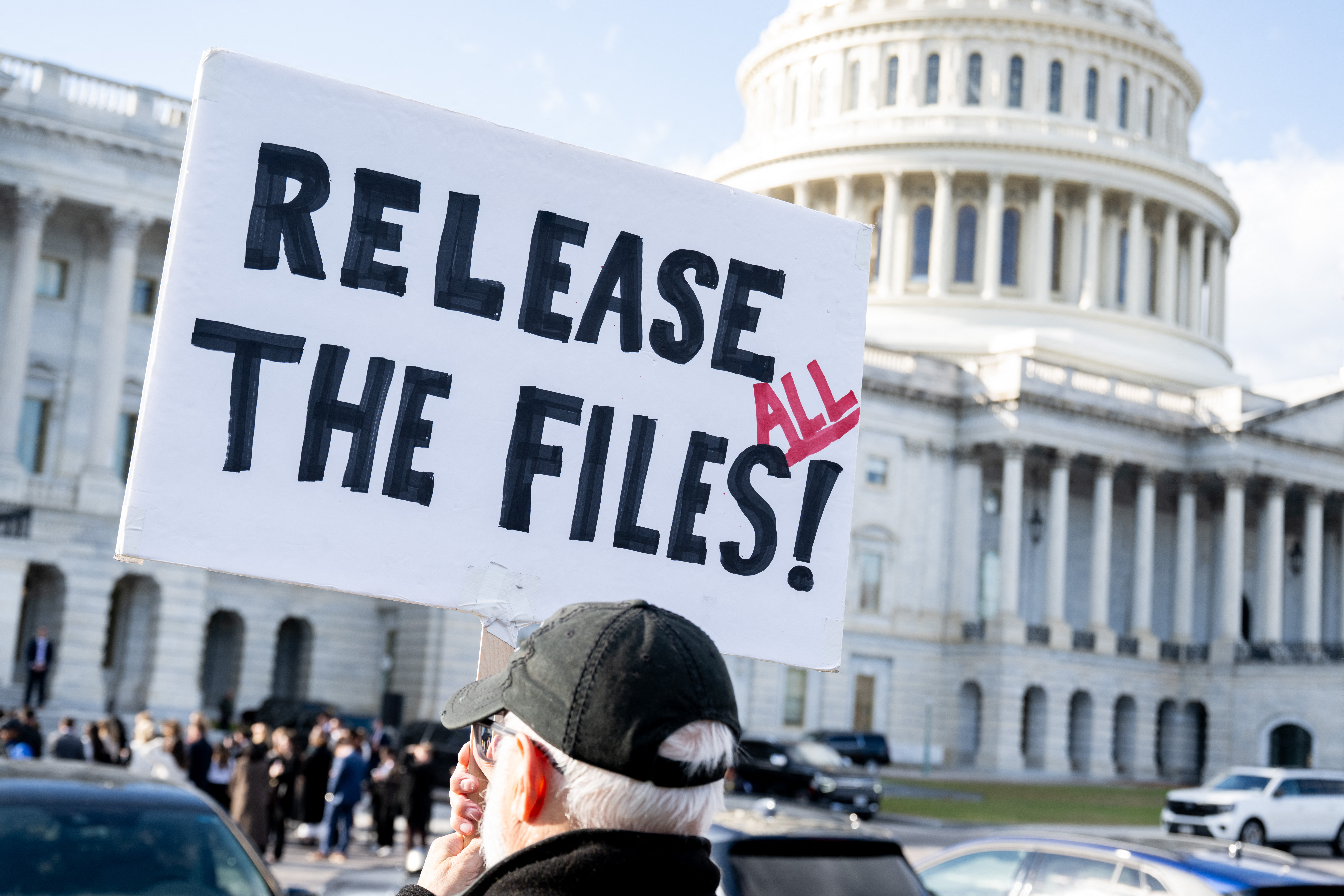 A protester holding a sign that says "RELEASE THE FILES!" with "ALL" in red, outside the US Capitol.