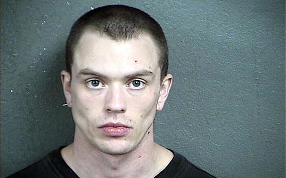 A police booking photo of a man with close-cut dark hair, seen from the neck up, in front of a green wall.