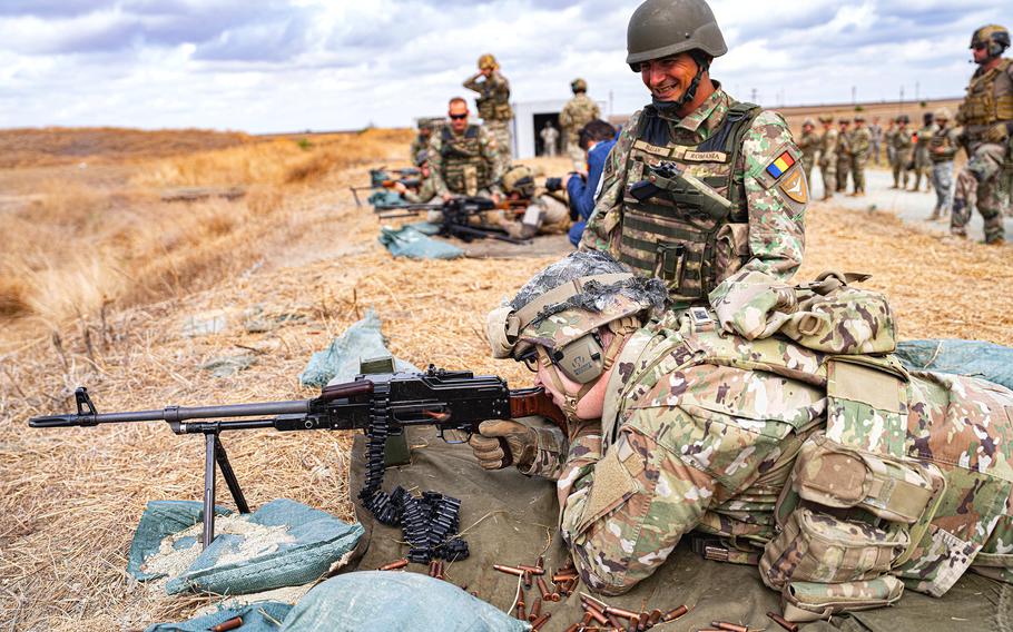 A Romanian soldier watches an American soldier fire a machine gun.