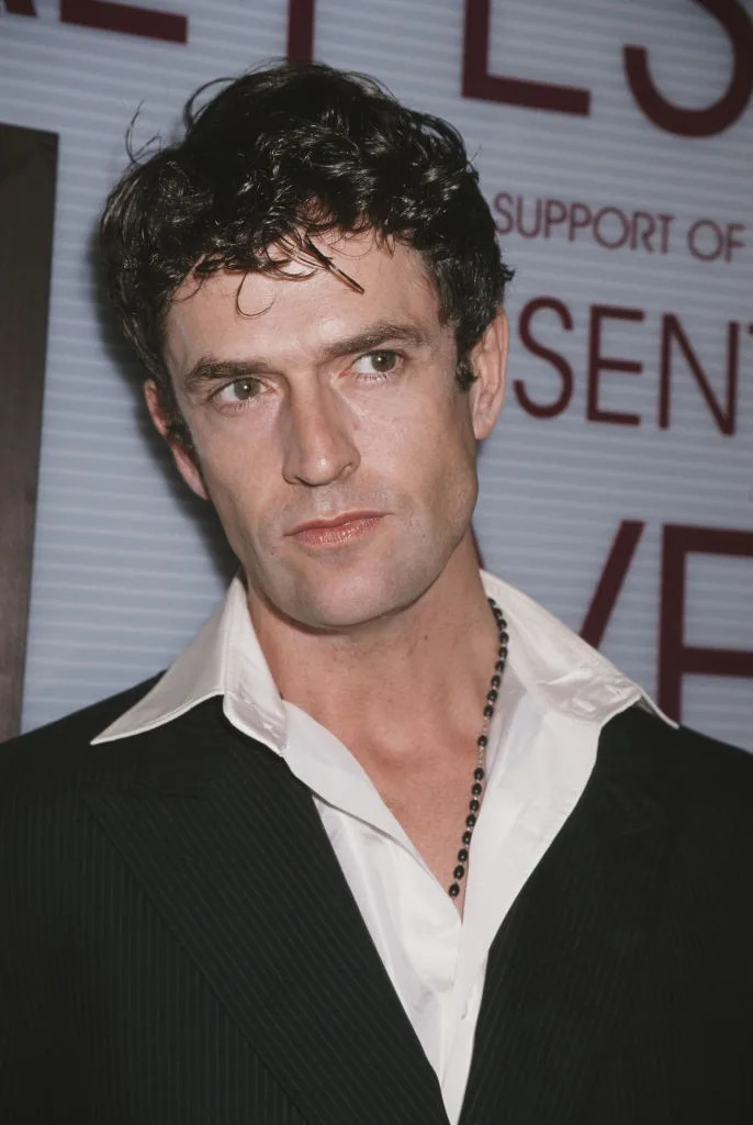 A person in a classic black suit with a white collared shirt at a formal event