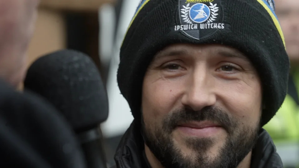A close up of Danny King as he is interviewed. He wears a black beanie hat with Ipswich Witches' logo on it. He has a dark black beard. 