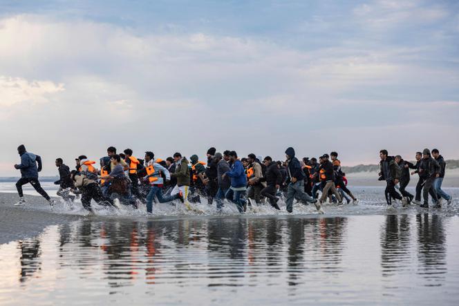 Migrants run to board a smuggler's boat in an attempt to cross the English Channel off the beach of Gravelines, northern France on August 12, 2025. 