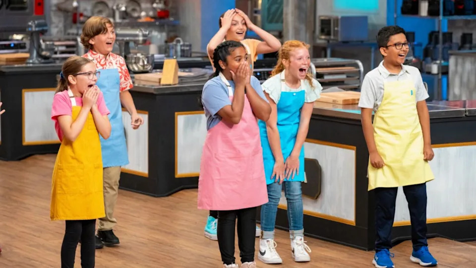 Children in aprons appear excited and surprised in a kitchen setting, likely participating in a cooking or baking competition show