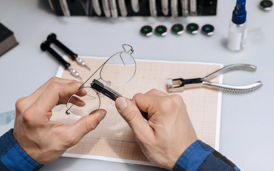 Two hands are working on a pair of metal framed eyeglasses over a white work space.
