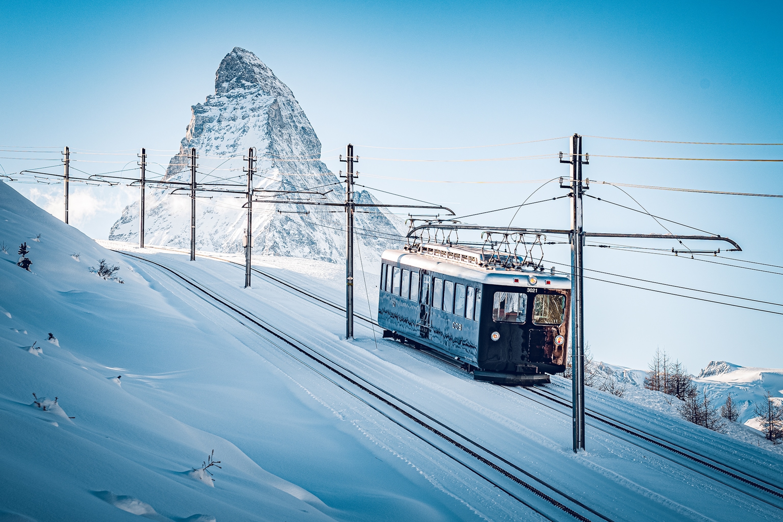 A small train carriage travels up a snowy mountain, with the Matterhorn in the background.