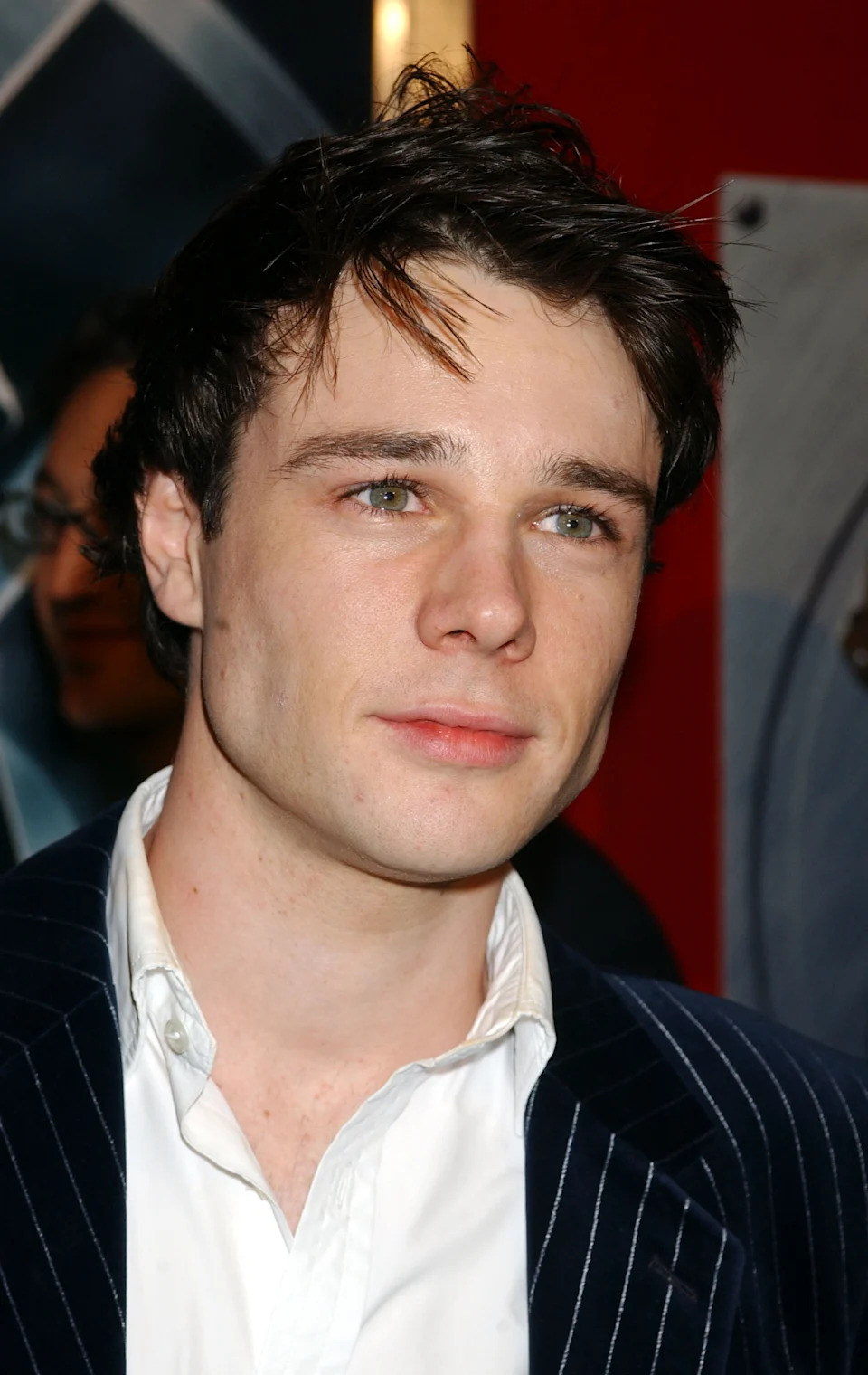 Person with short hair in a pinstripe suit and white shirt at a public event