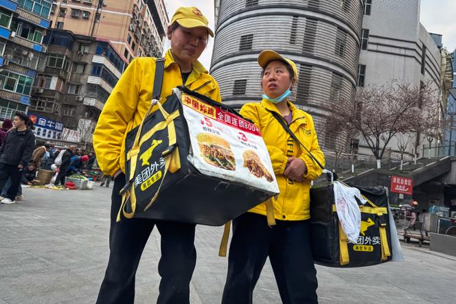 Two food delivery workers crossed a square while promoting discounts on menus offered by the Meituan platform, in Chongqing, Sichuan province, on March 10, 2025.