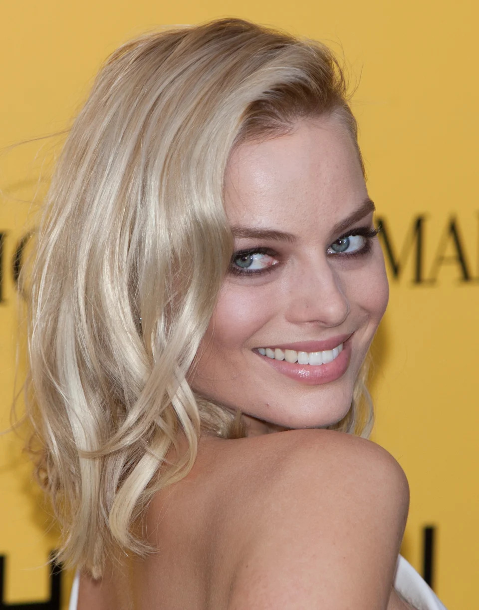 I don't know who this is, but they're smiling at a premiere, wearing a strapless gown, with wavy hair styled to one side