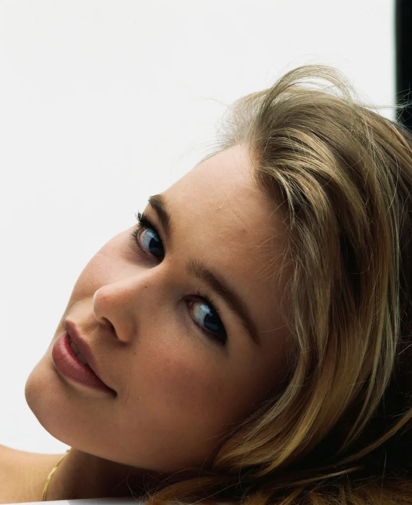 A person with long hair smiles gently, their face angled slightly upwards