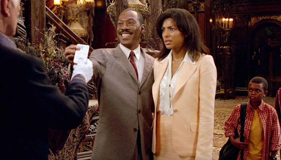 A man in a suit and a woman in a blazer are smiling inside a grand, ornate room. A child stands nearby, looking to the side