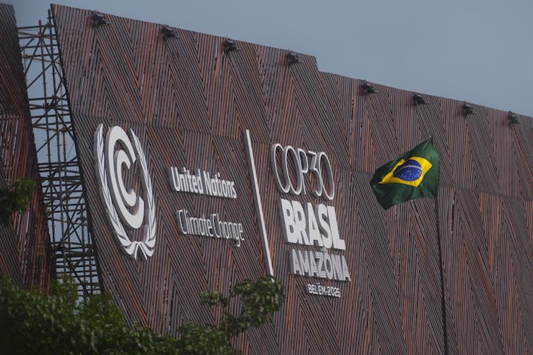 the flag of brazil on a pole next to a building with the words COP 30 Brasil written on it in large letters
