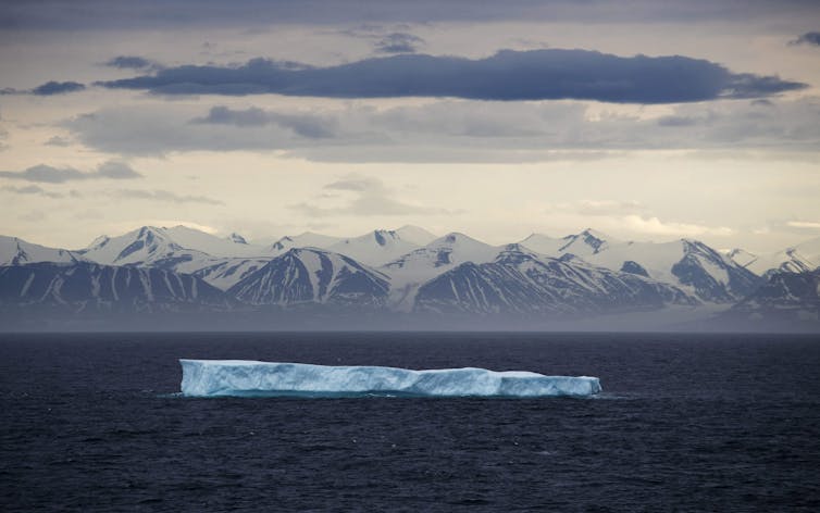 an iceberg floating in the ocean, snowcapped mountains in the background