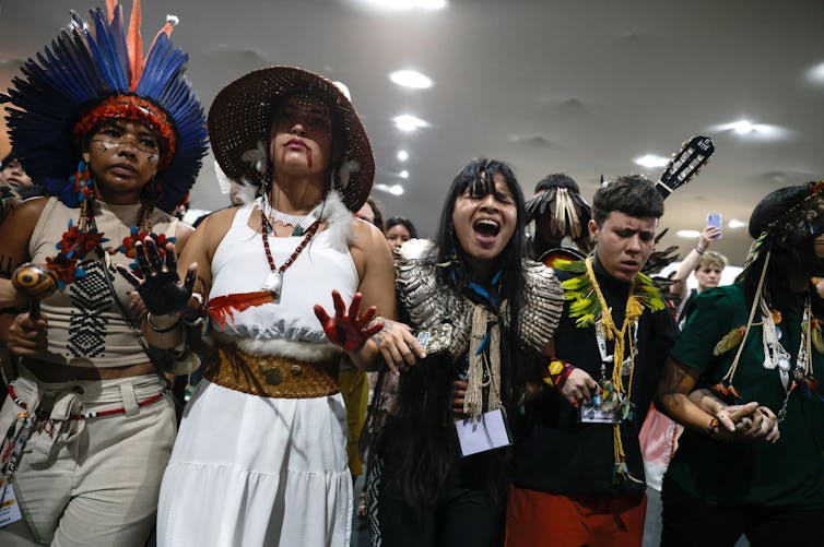 A line of protestors holding hands and shouting, wearing Indigenous jewellery
