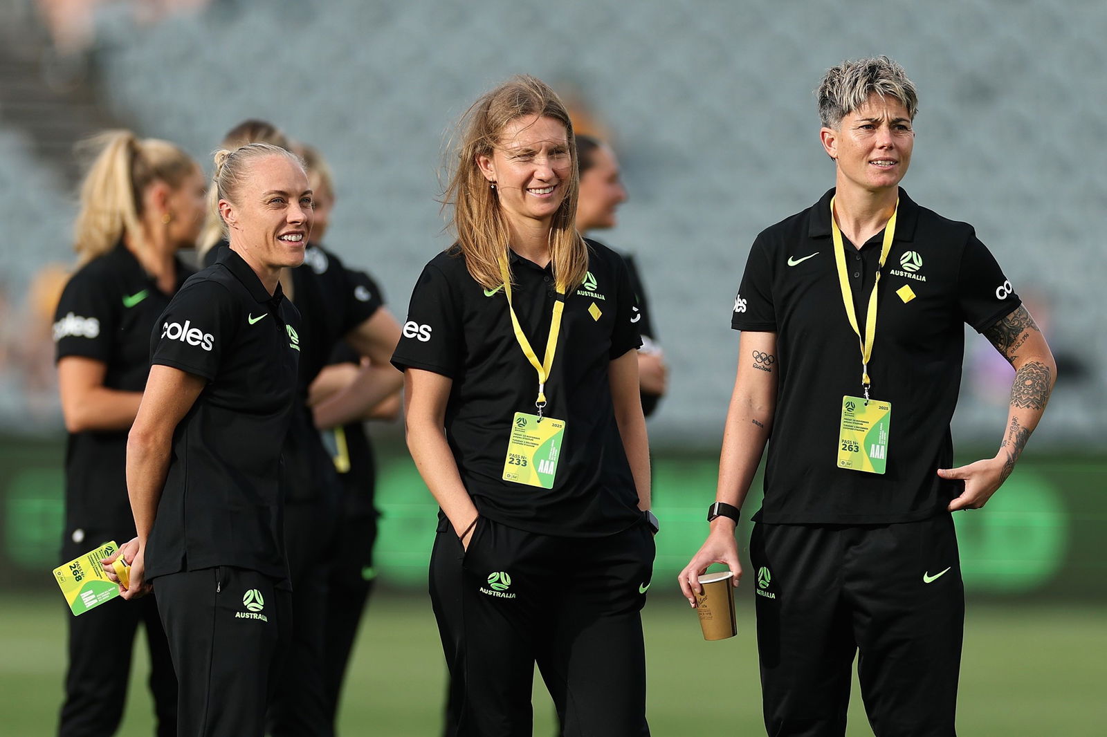 Three soccer players in dark blue training outfits smile.