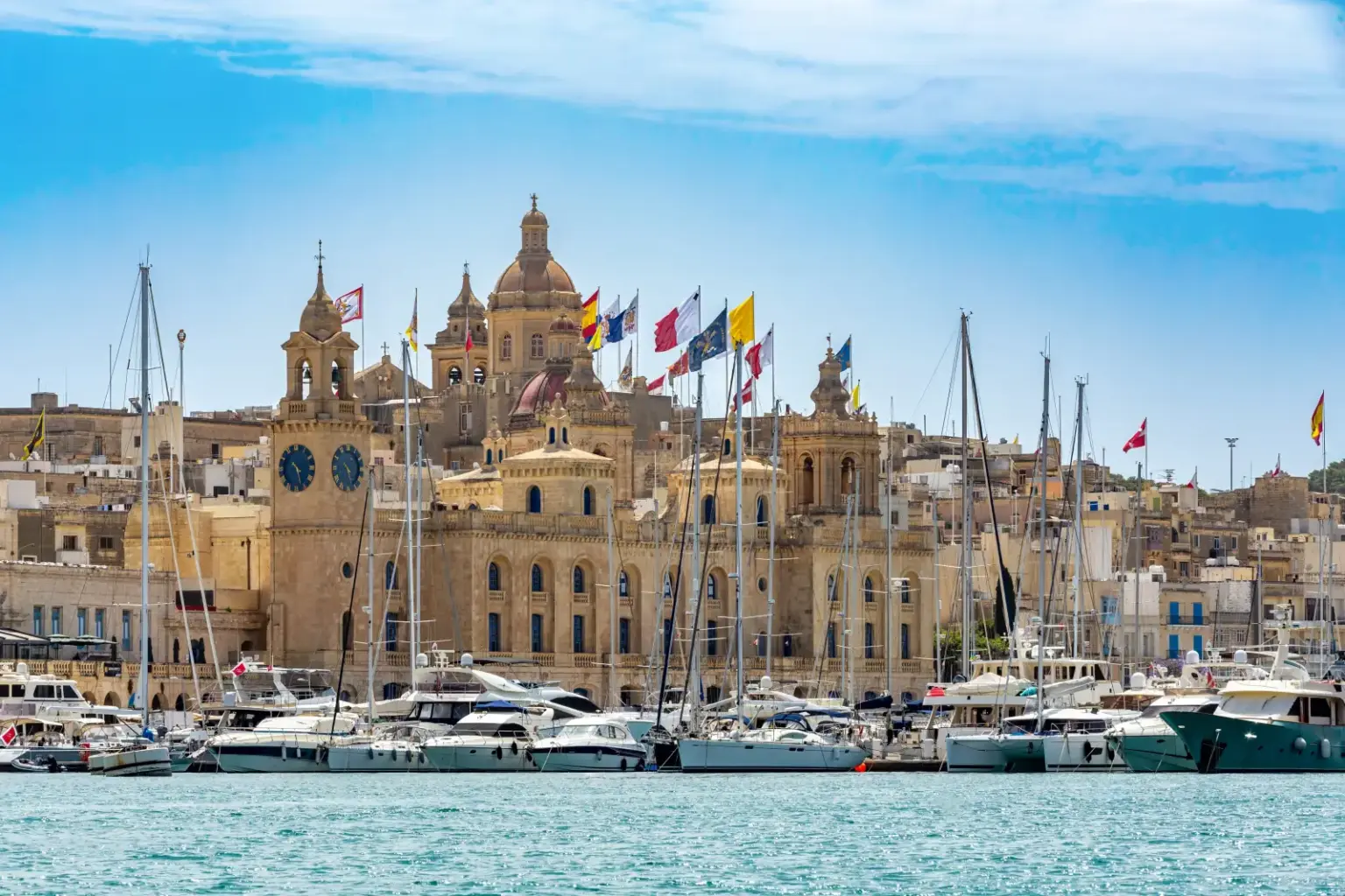 Birgu and Vittoriosa skyline in Malta with historic limestone buildings, church domes and a marina of anchored boats.