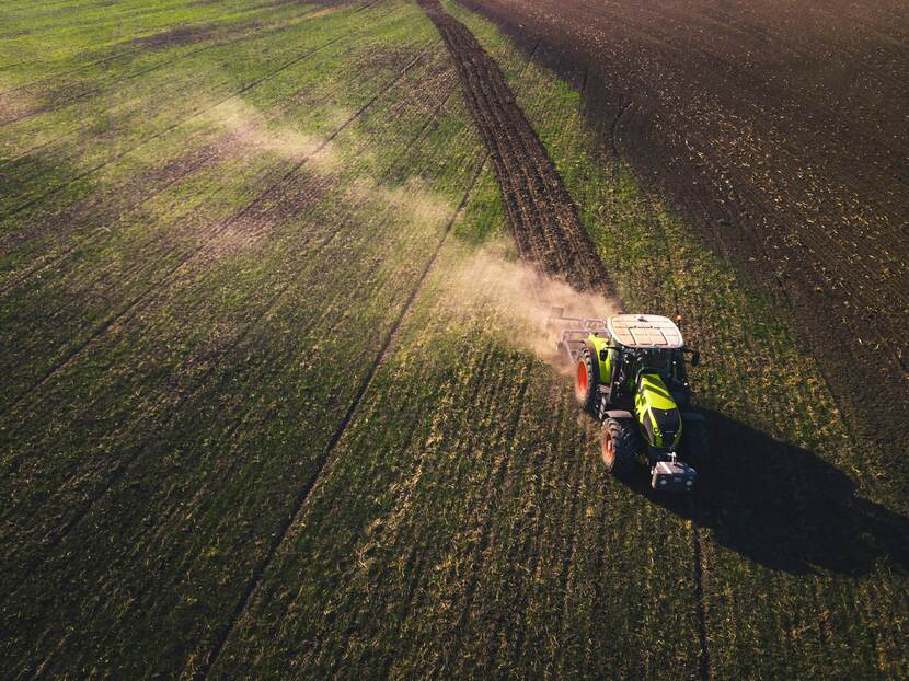 A tractor working in a vast open field under a clear sky, preparing the soil for planting.