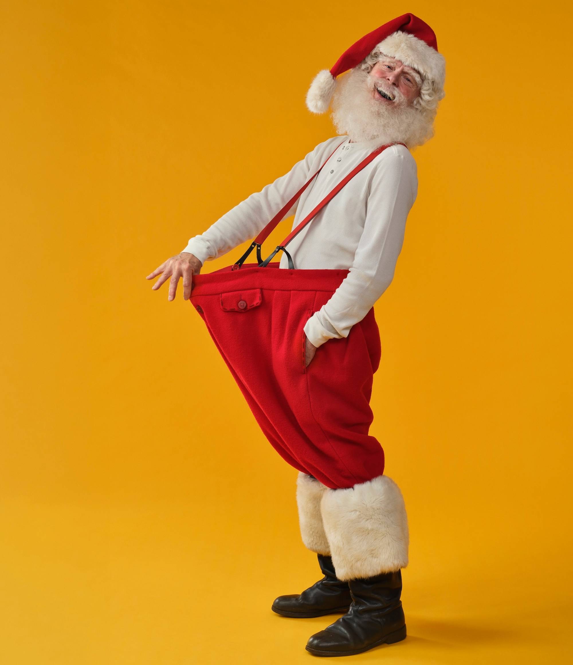 Santa Claus holding out his oversized red pants to show how much weight he's lost.