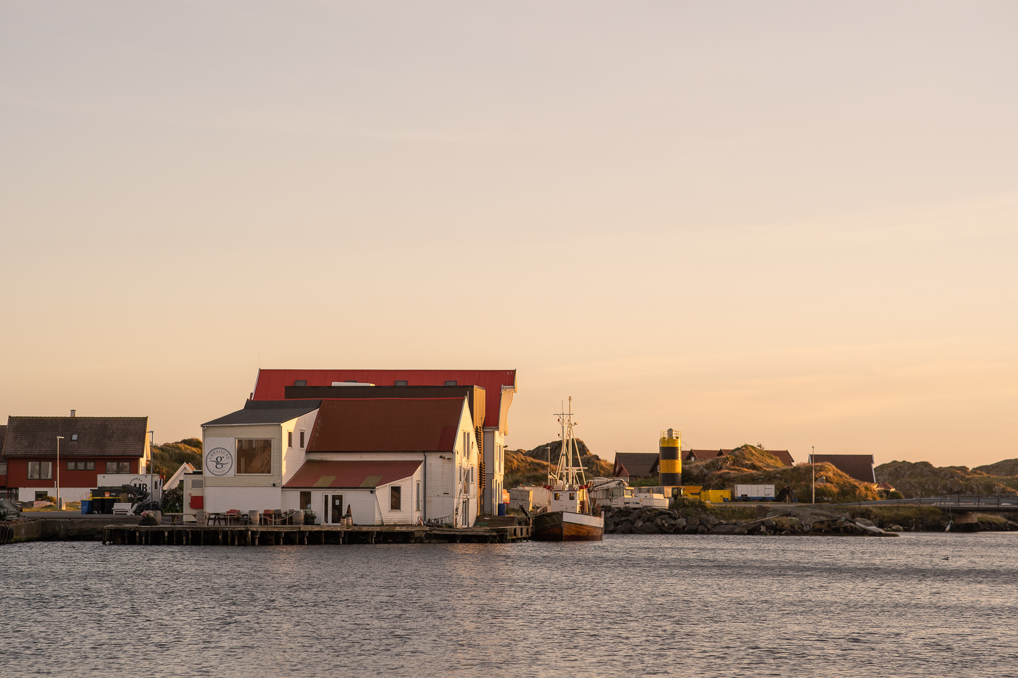 Kvitsoy harbor at sunset, with buildings and a boat by the water.