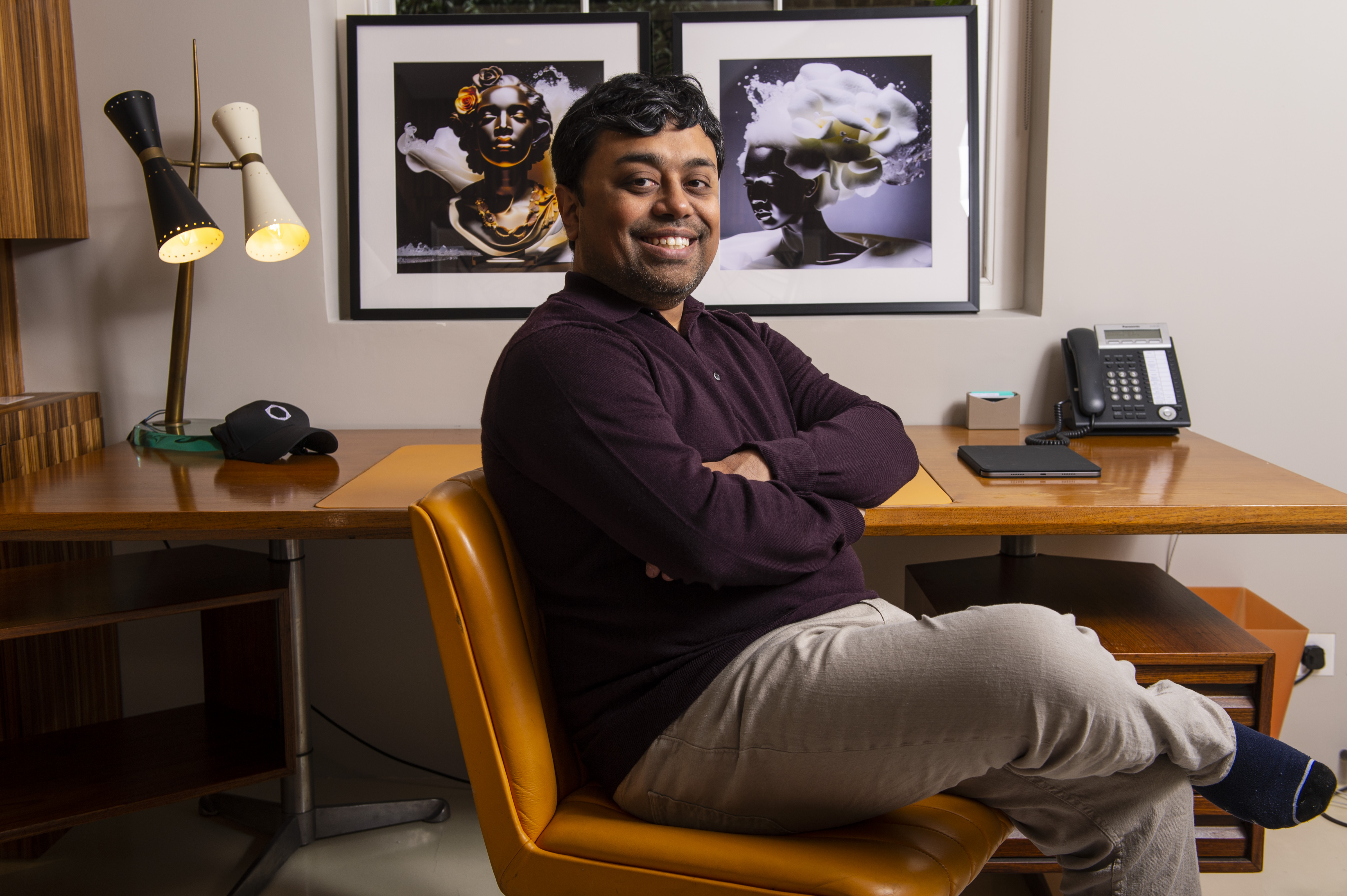 Emad Mostaque, founder and CEO of Stability AI, seated at a desk with AI-generated images on the wall.