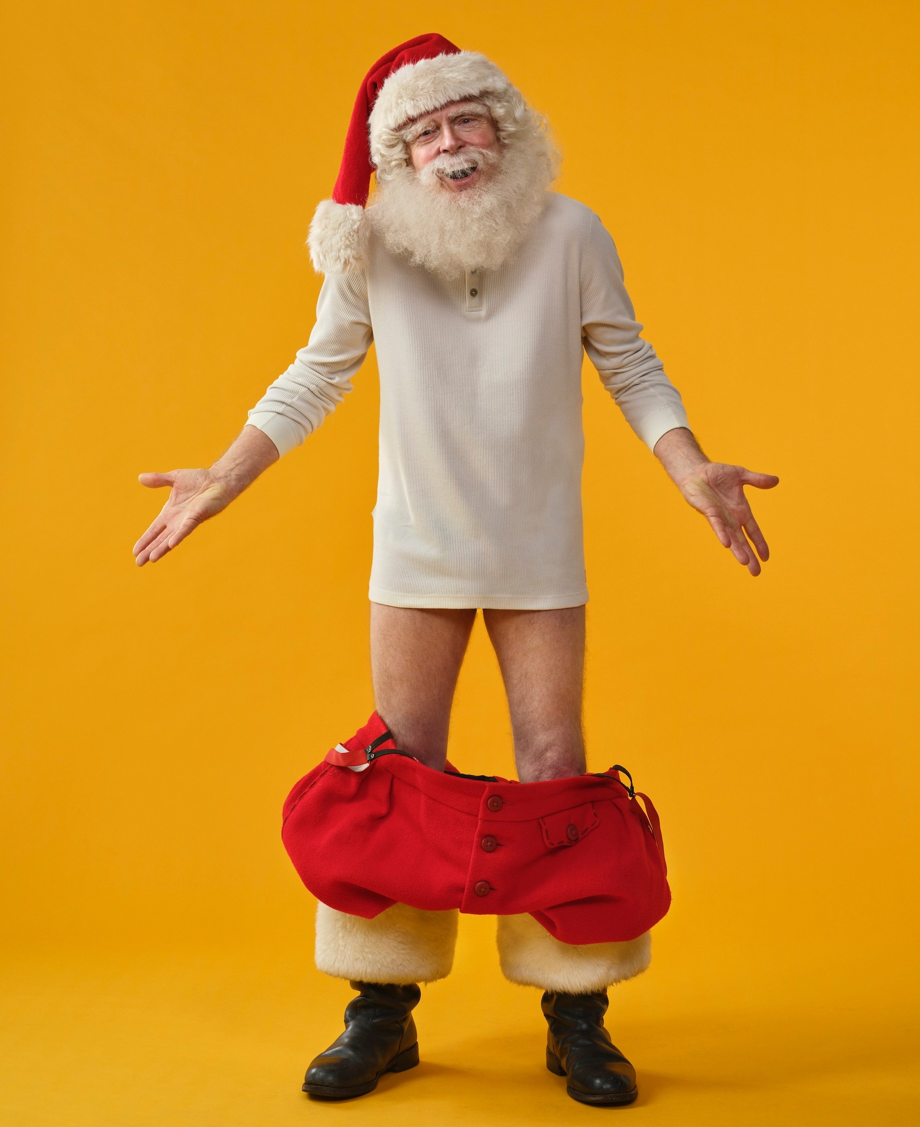 Santa Claus in a red hat and white shirt with his red pants around his ankles.