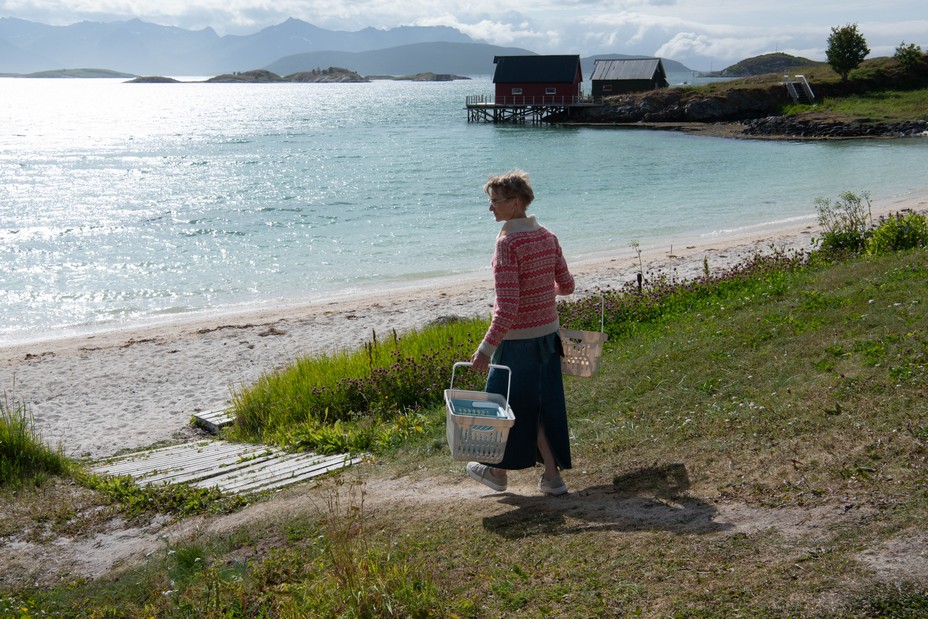 A color photograph of a woman carrying large baskets while walking to the beach