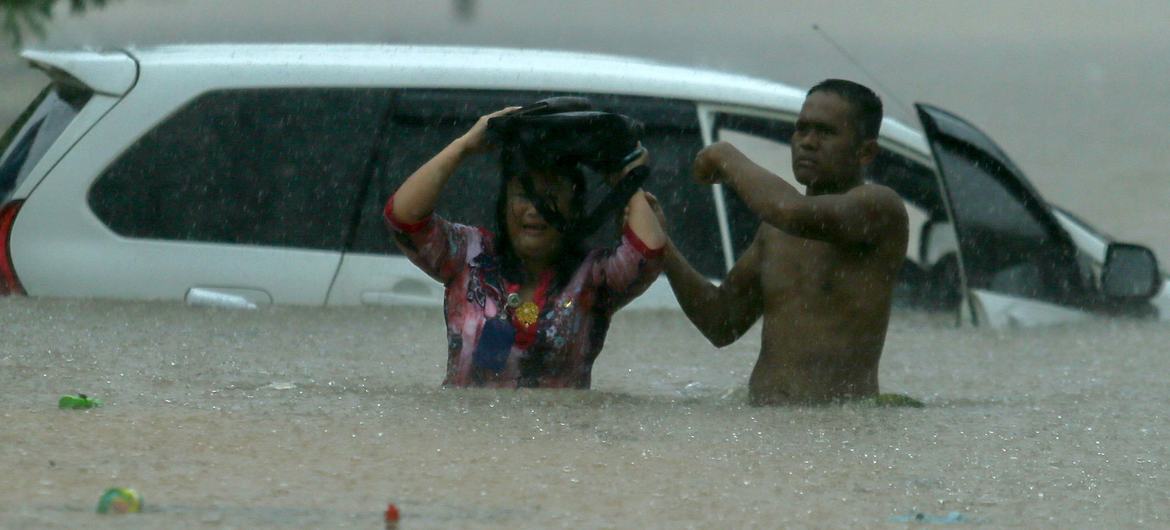 A man helps a woman after her car is stranded in waist-deep water. Globally rains are being more extreme due to impacts of climate change.