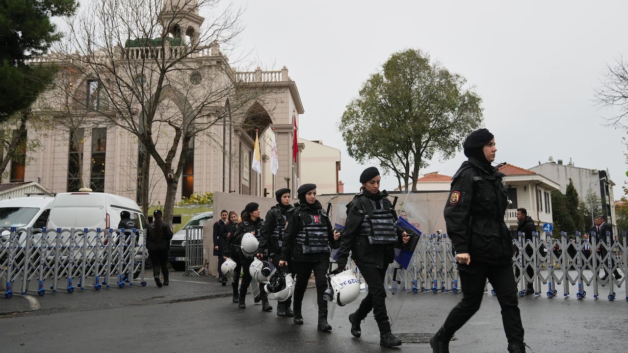 People in black outfits and carrying helmets walk across a street 