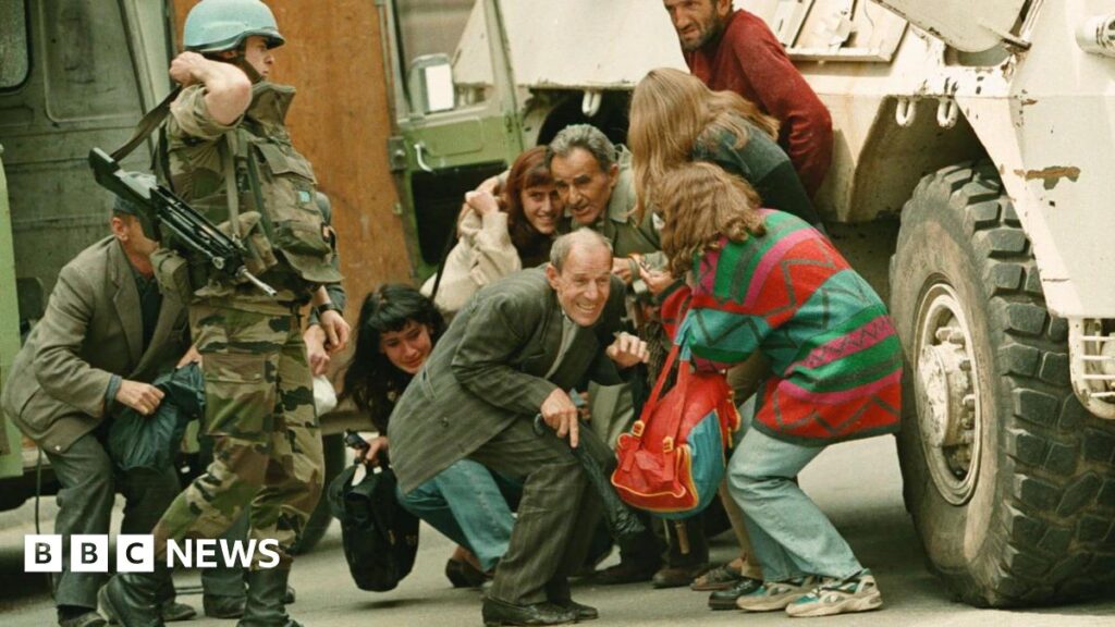 A French U.N. soldier stands alongside a group of Sarajevans seeking shelter behind a French U.N. armoured personnel carrier from sniper-fire after being rescued from their van by French U.N. peacekeepers at a dangerous Sarajevo intersection Thursday June 8, 1995.