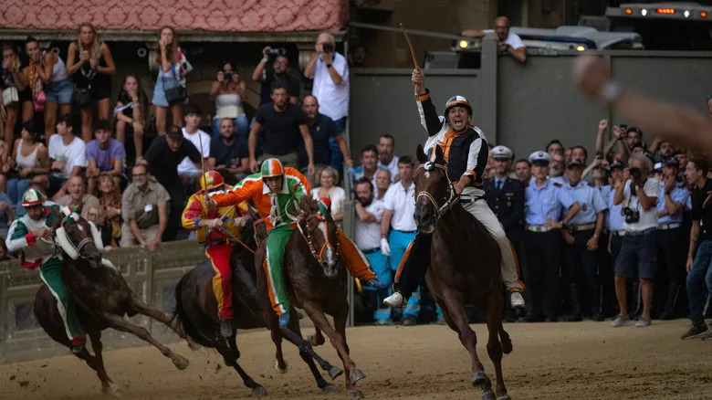 Horses and jockeys in the Palio horse race, with crowds in the background