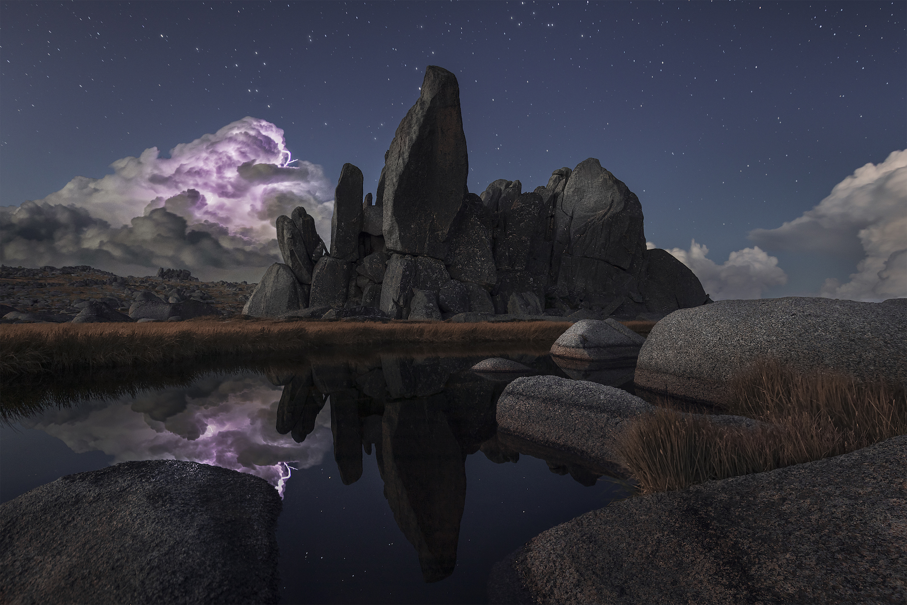 storm cloud with purple lightning moves over horizon. rock formations and reflective lake in foreground
