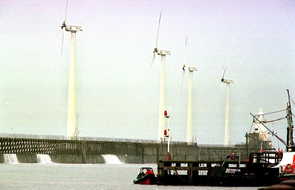 A photo of the wind turbines being built in Blyth. There is a large concrete structure supporting four turbines. A black vessel with the name "Bernica Newcastle" is next to it.