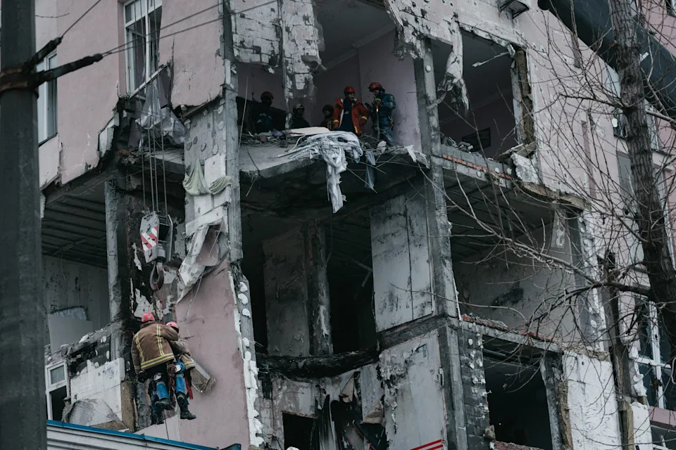 Emergency services hanging from a crane clear dangerous debris from the facade of the struck building on Hotkevycha Street in Kyiv, Ukraine on December 27, 2025. The attack, carried out by a Russian Shahed drone, damaged the lower floors of a high-rise building and injured several civilians.