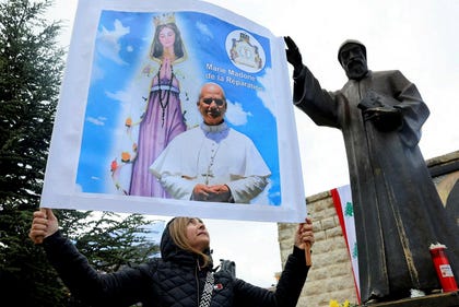 A woman holds up a placard with the images of Pope Leo XIV and "Mary, Madonna of Reparation" next to a statue of St Charbel on the day Pope Leo XIV visits the Monastery of Saint Maroun, in Annaya, Lebanon on Monday.