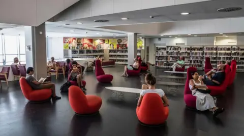 Getty Images About a dozen people are seen sitting or reading on chairs in a library during a heatwave in Barcelona