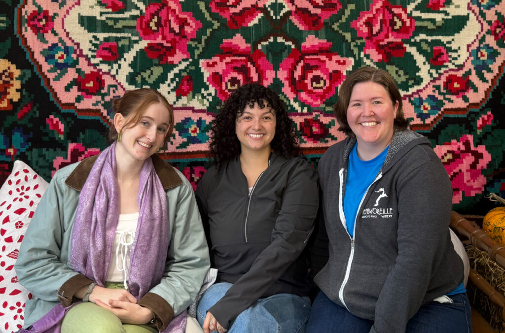 WSU students Cecilia Sevier, Mackenzie Aragon, and Julie Hilland posing for a group photo beneath a floral wall hanging.