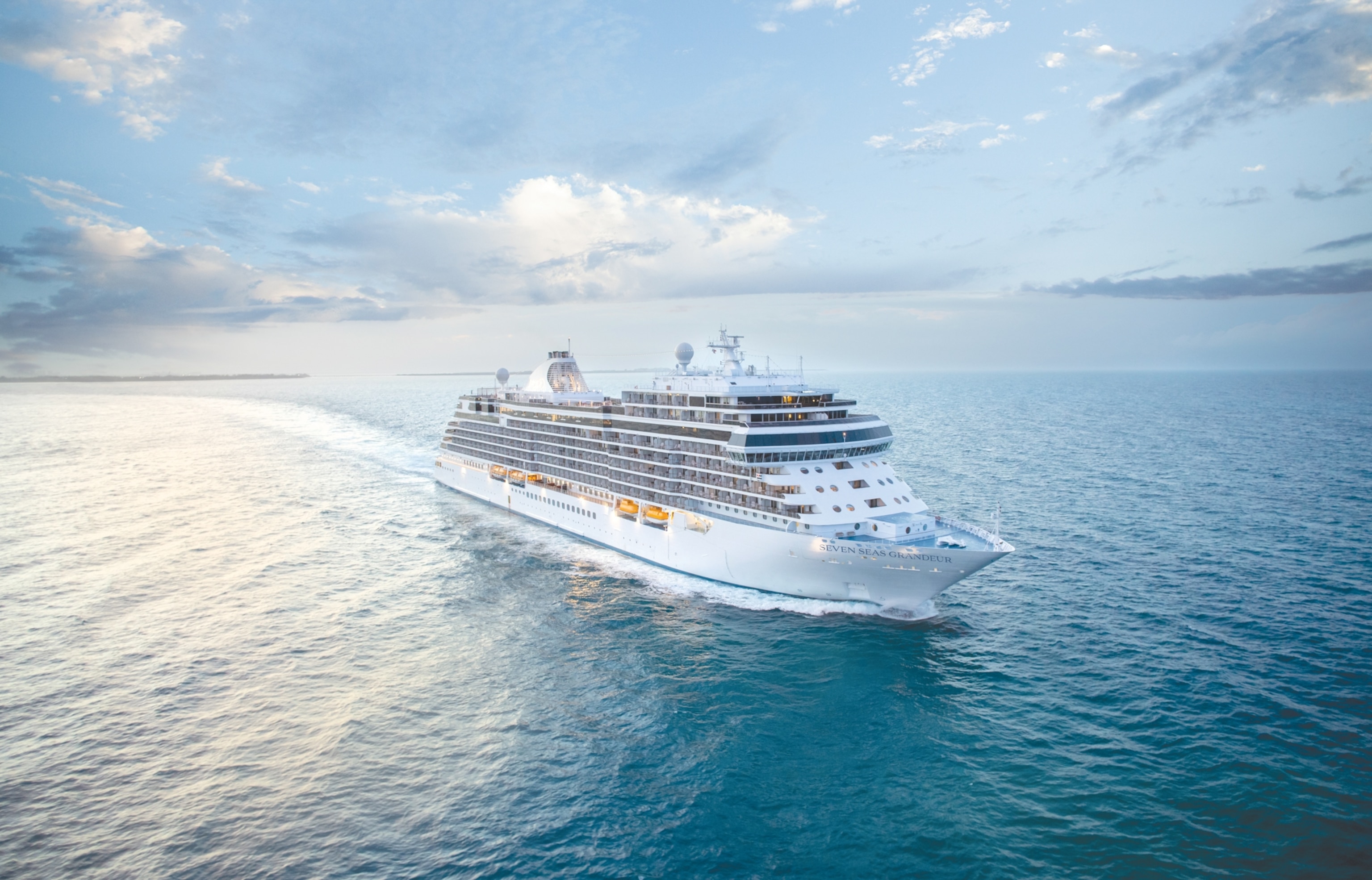 A large cruise ship sails smoothly through calm, blue ocean waters under a partly cloudy sky, creating a serene and adventurous atmosphere.