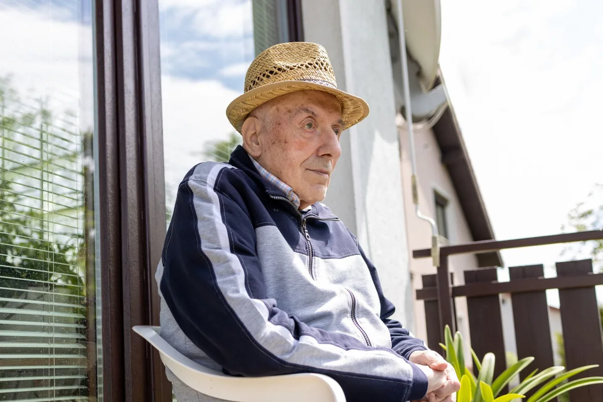 An old man sits outside on a chair