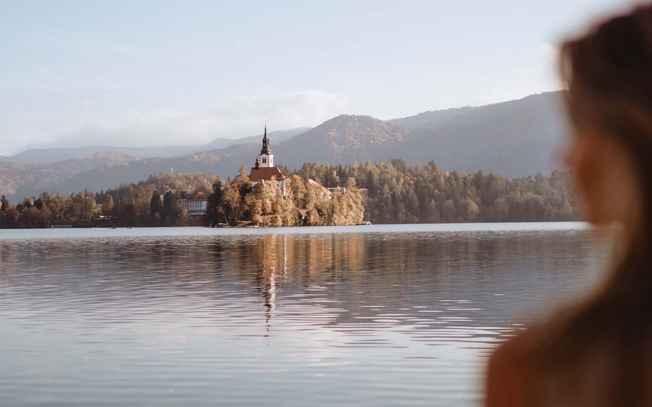 Woman overlooking lake with view of church in Slovenia on Porsche Travel Experience