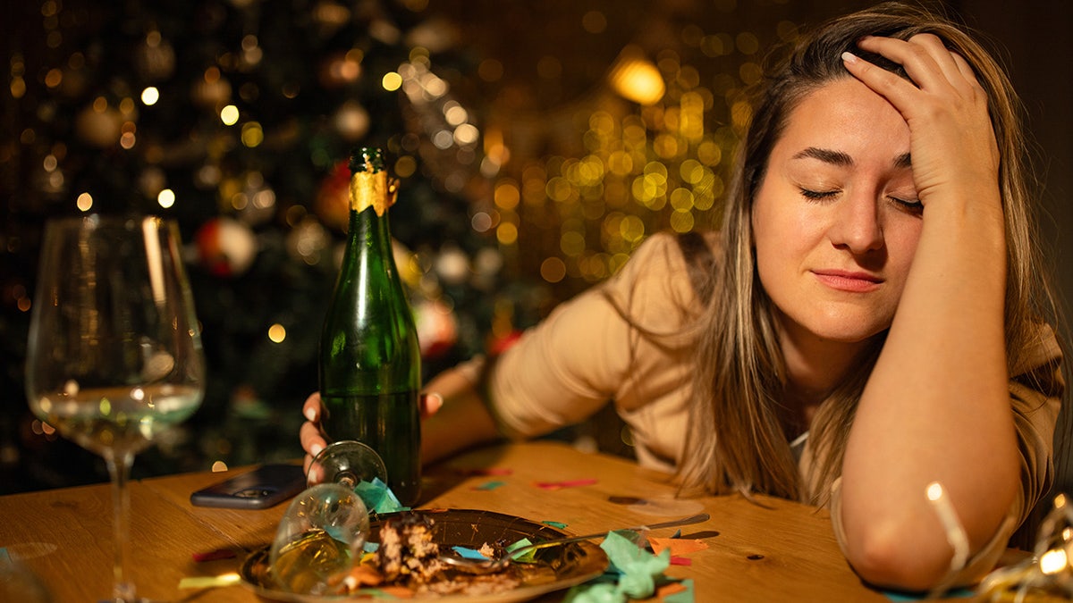 Woman seen slumped over on bar during holidays, champagne bottle and glass seen in front of her.