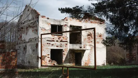 Stu McKenzie The shell of a derelict home in Bosnia, with no windows or doors, no roof and loose bricks throughout.