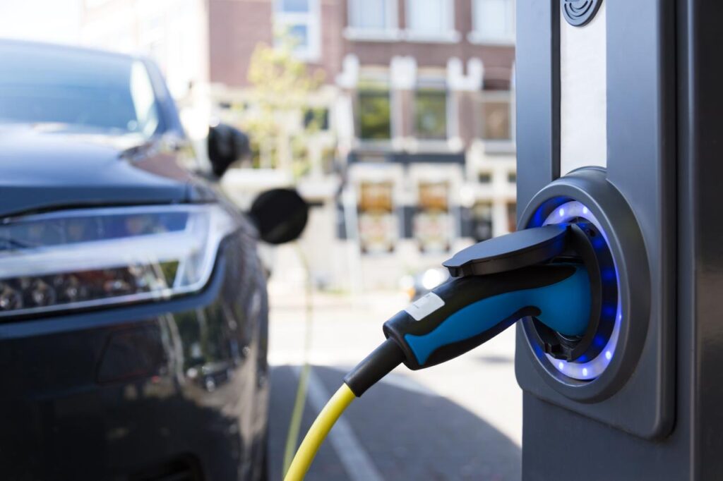 Photo shows a view of an electric car charging column and in the background a partial view of a car, accessed on Dec. 18, 2025. (Adobe Stock Photo)