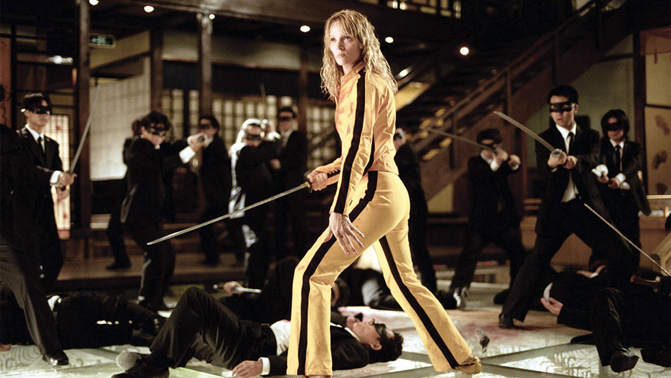 woman in a yellow outfit wielding a sword surrounded by attackers in suits