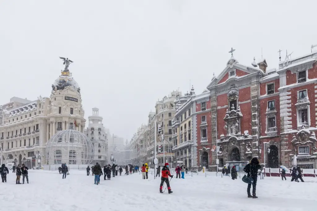 Snow-covered Gran Vía in Madrid with pedestrians walking during a winter storm.