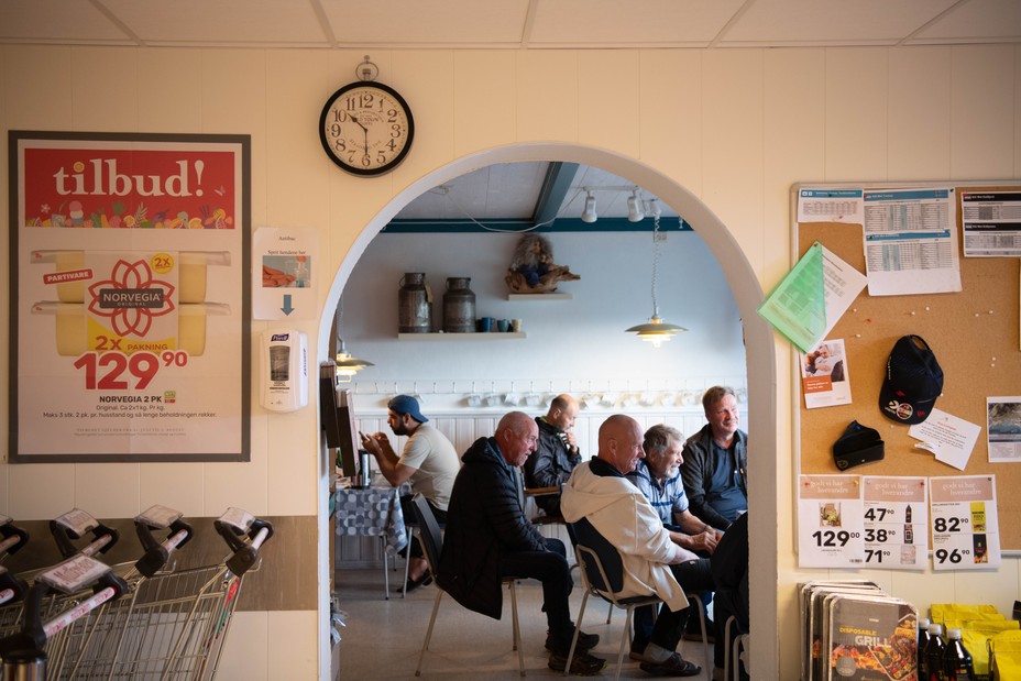 A photograph of local men gathering at a small grocery store. There is a clock on the wall