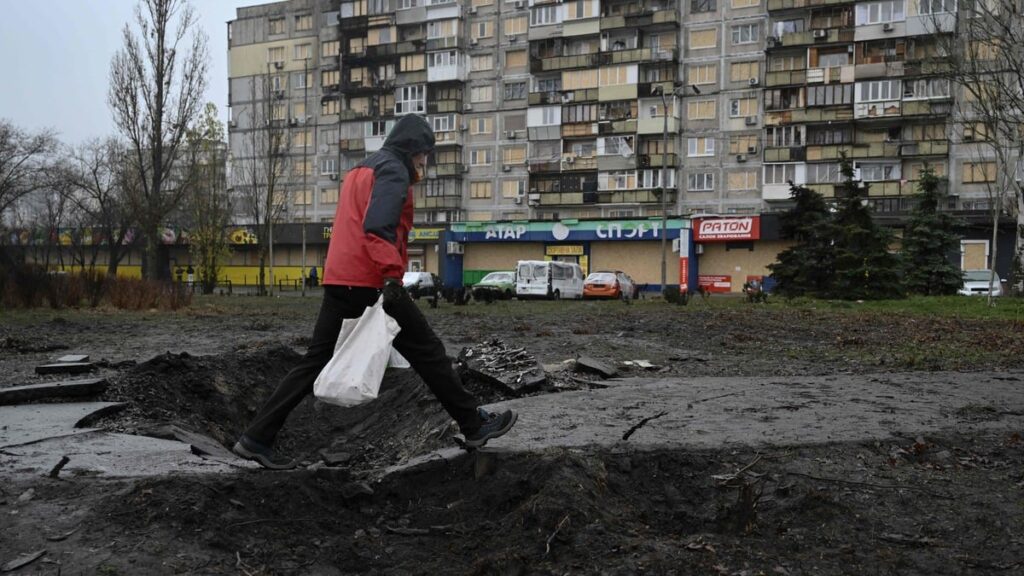 A man walks over a crater in front of a residential building damaged after a recent air attack, in Kyiv on December 3, 2025.