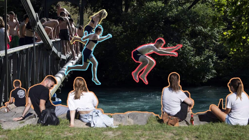 People sit on the grassy bank of a river, watching others jump off a low bridge into water. They people are outlined in different bright coloures.