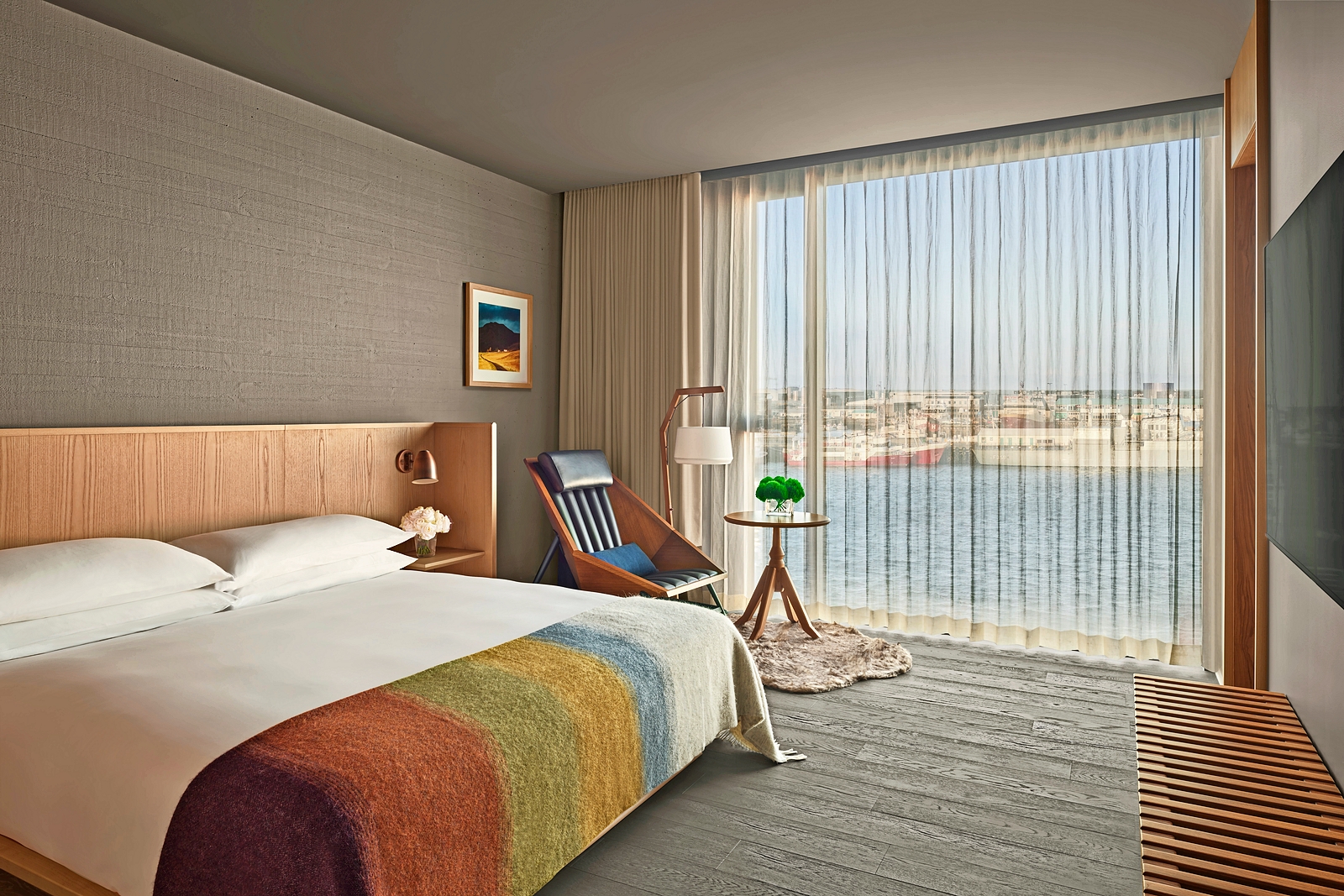 A bedroom in The Reykjavik EDITION with a king bed, lounge chair, and harbor view.